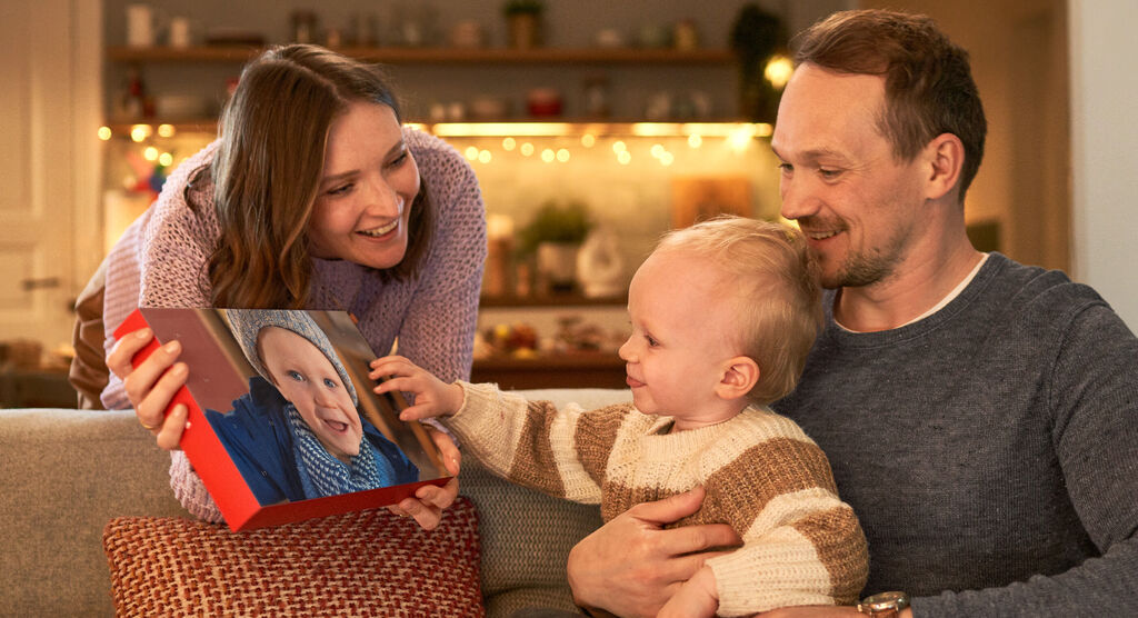 Una familia sentada en una sala acogedora mirando un álbum de fotos con un niño feliz.