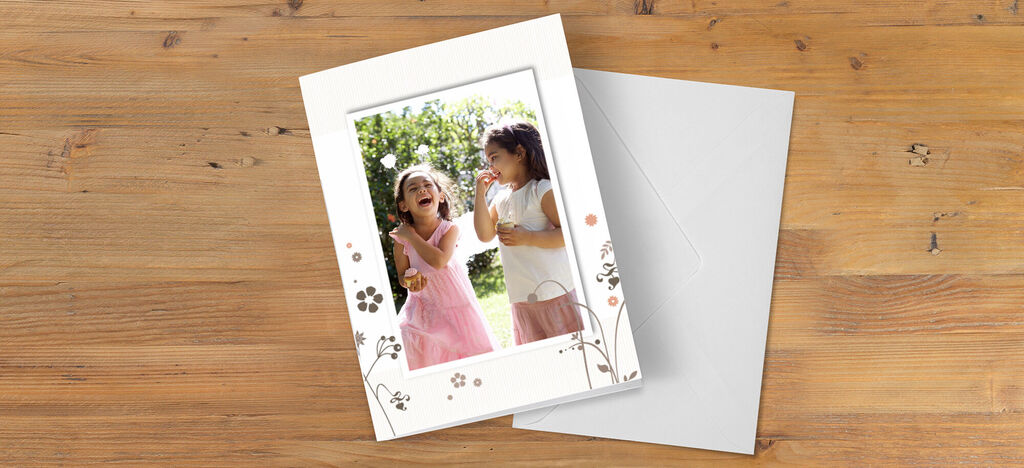 Dos niñas alegres riendo y jugando al aire libre, rodeadas de flores en una tarjeta.