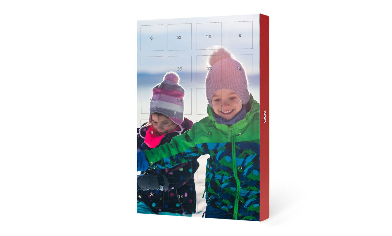Dos niños alegres sentados juntos junto a un calendario de Adviento en la nieve.