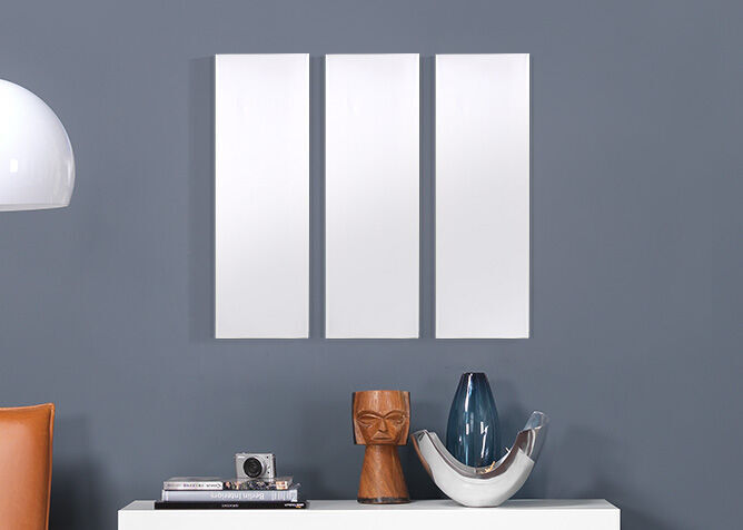 Tres marcos vacíos blancos en una pared gris sobre un mueble decorativo.