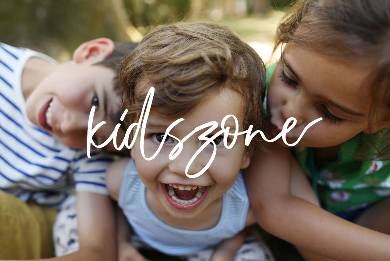 Tres niños están sentados alegremente al aire libre mirando algo en el frente.