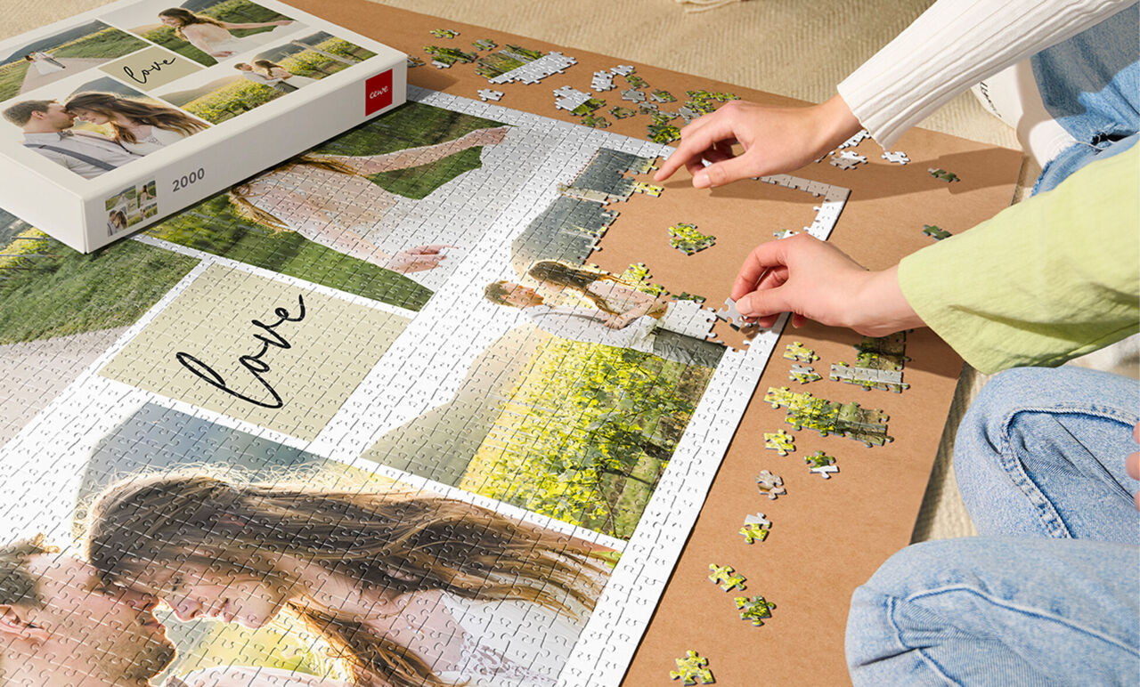 Manos de una persona armando un puzzle personalizado de fotos de pareja sobre una mesa, junto a su caja original.