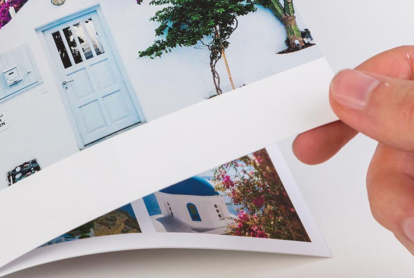 Mano pasando la página de un álbum de fotos con imágenes de casas blancas y puertas de colores al estilo mediterráneo