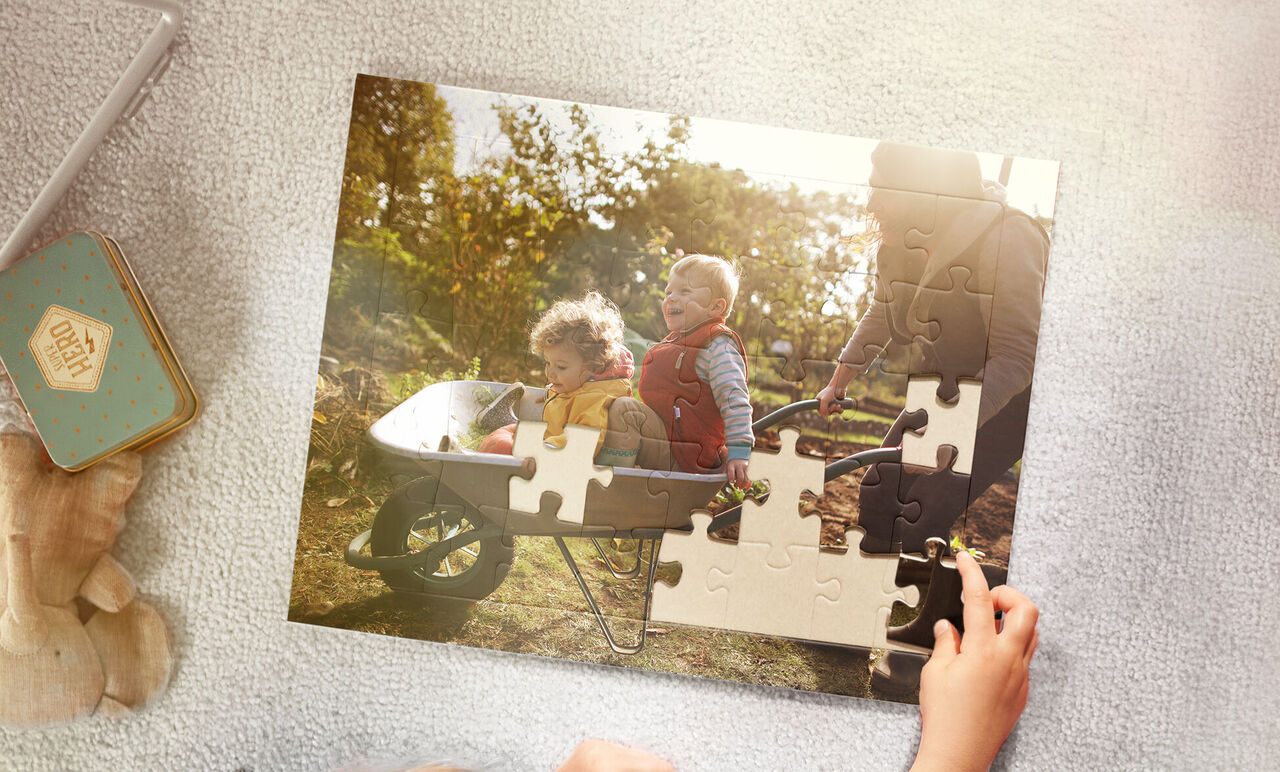 Dos niños y un adulto armando un rompecabezas al aire libre, con una carretilla al fondo.