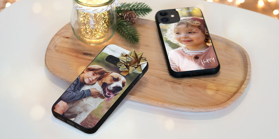 Dos fundas de smartphone con diseños fotográficos en una tabla de madera. Una muestra un perro y un niño, y la otra un diseño personal.