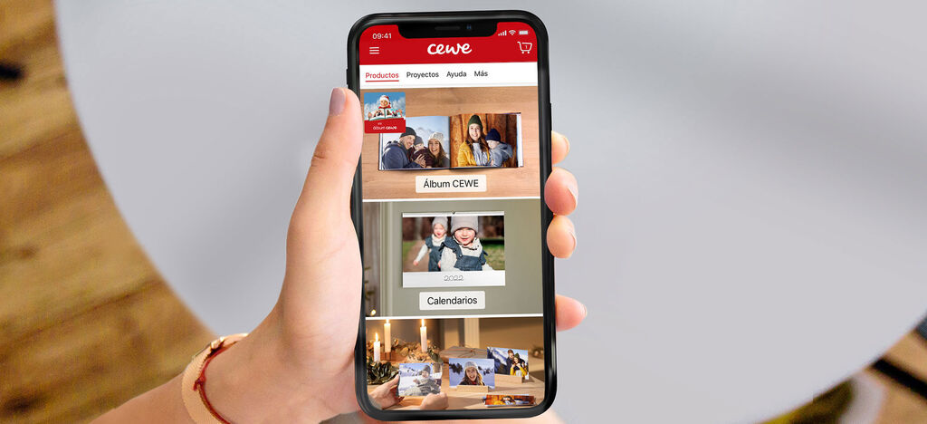 Una persona sostiene un smartphone que muestra la app CEWE con fotos en un álbum digital.