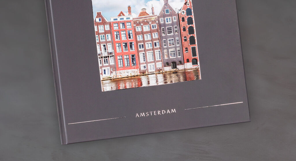 Un CEWE FOTOBUCH con una hermosa foto de casas coloridas en Ámsterdam sobre un fondo gris elegante.