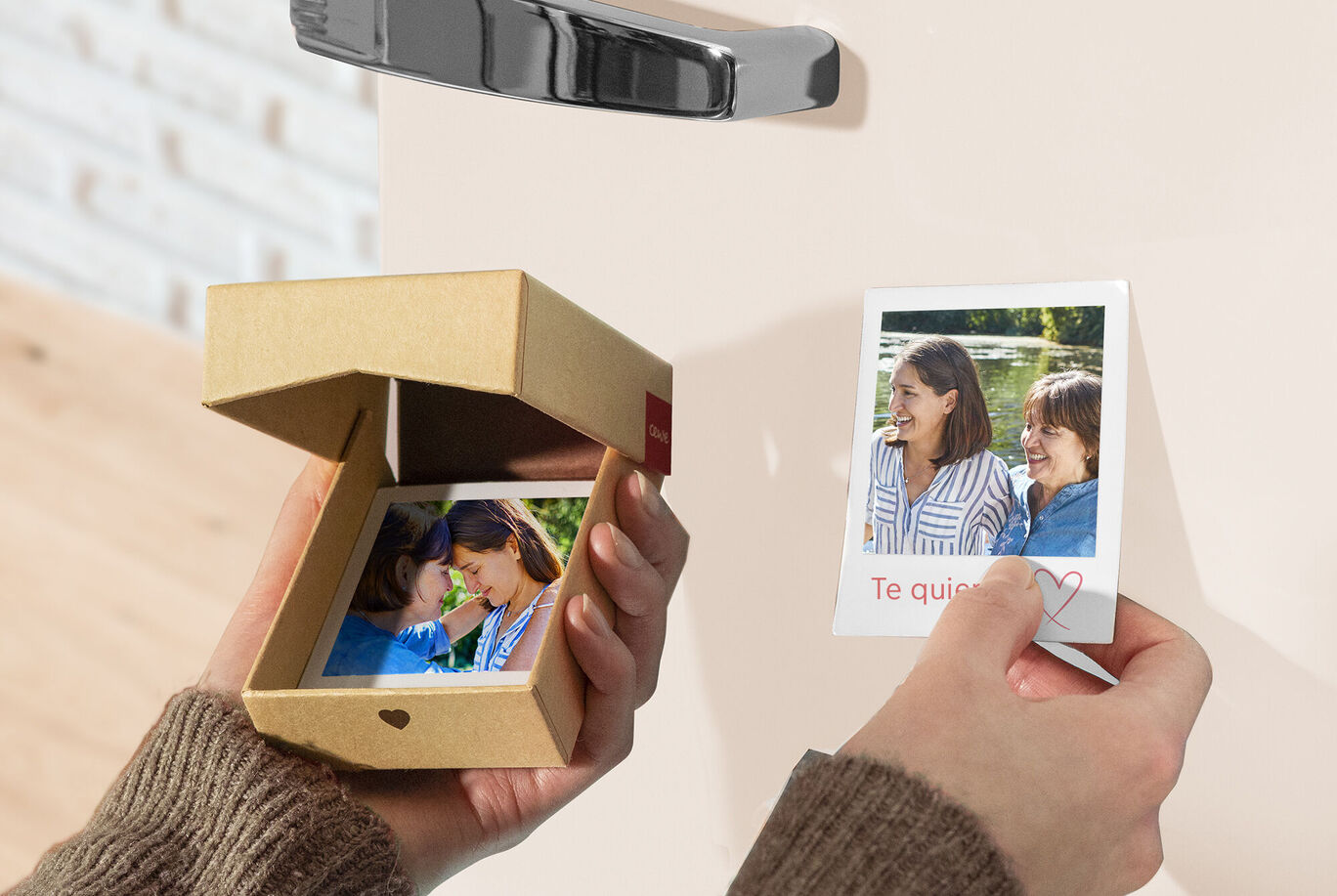 Una persona sostiene una pequeña caja de regalo con una foto dentro y una tarjeta de saludo.