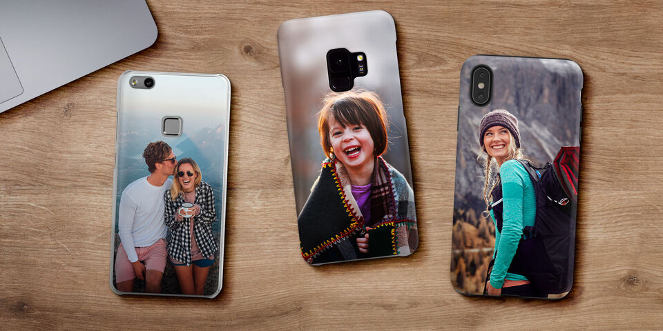 Tres móviles con fundas personalizadas sobre una mesa de madera.