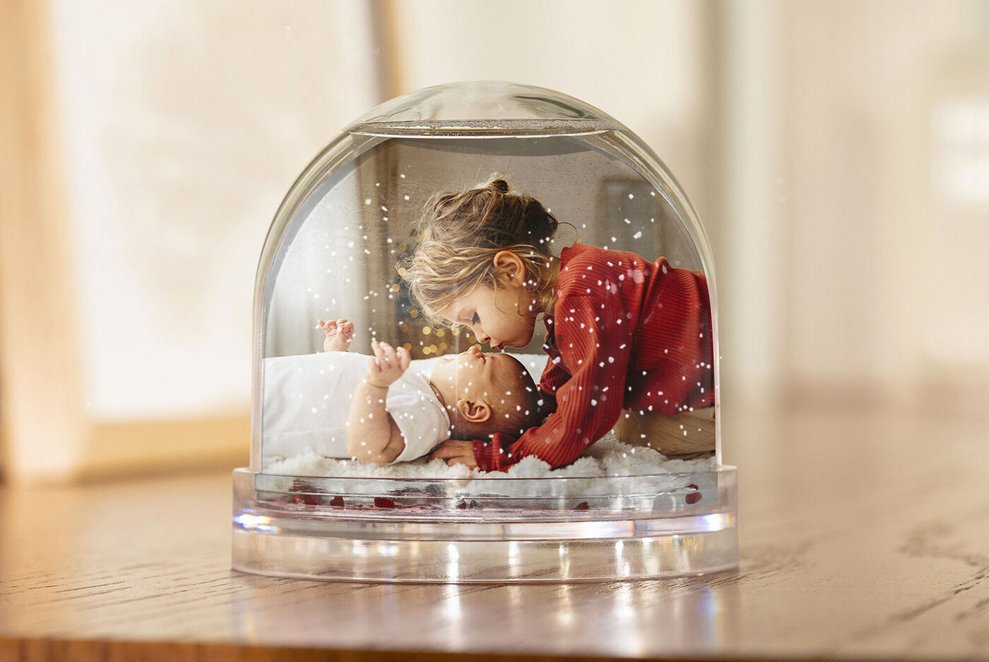 Dos niños bajo una bola de nieve en una habitación cálida. El mayor se inclina suavemente sobre el menor.