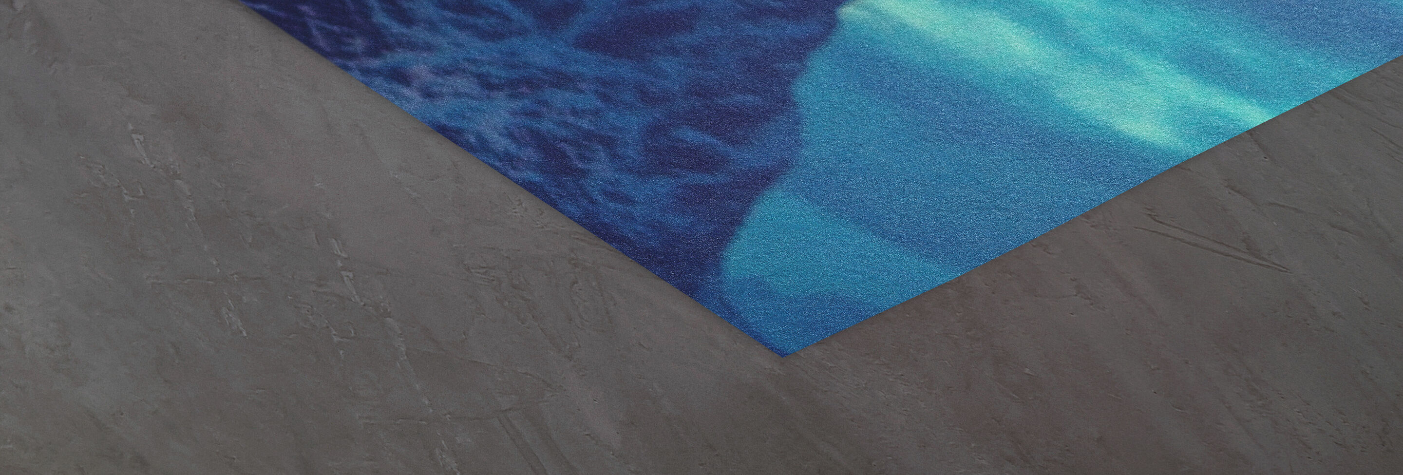 Detalle de una esquina textil azul con patrón sobre fondo gris.