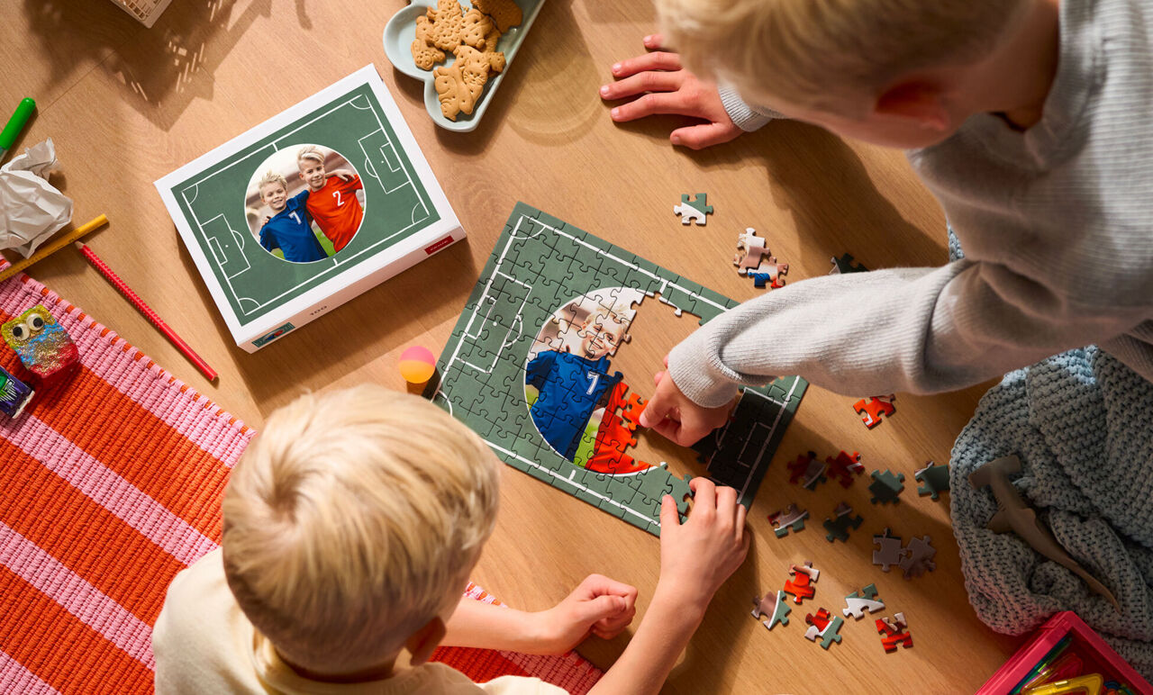 Vista superior de dos niños armando un puzzle personalizado con diseño de campo de fútbol y su foto, junto a la caja.