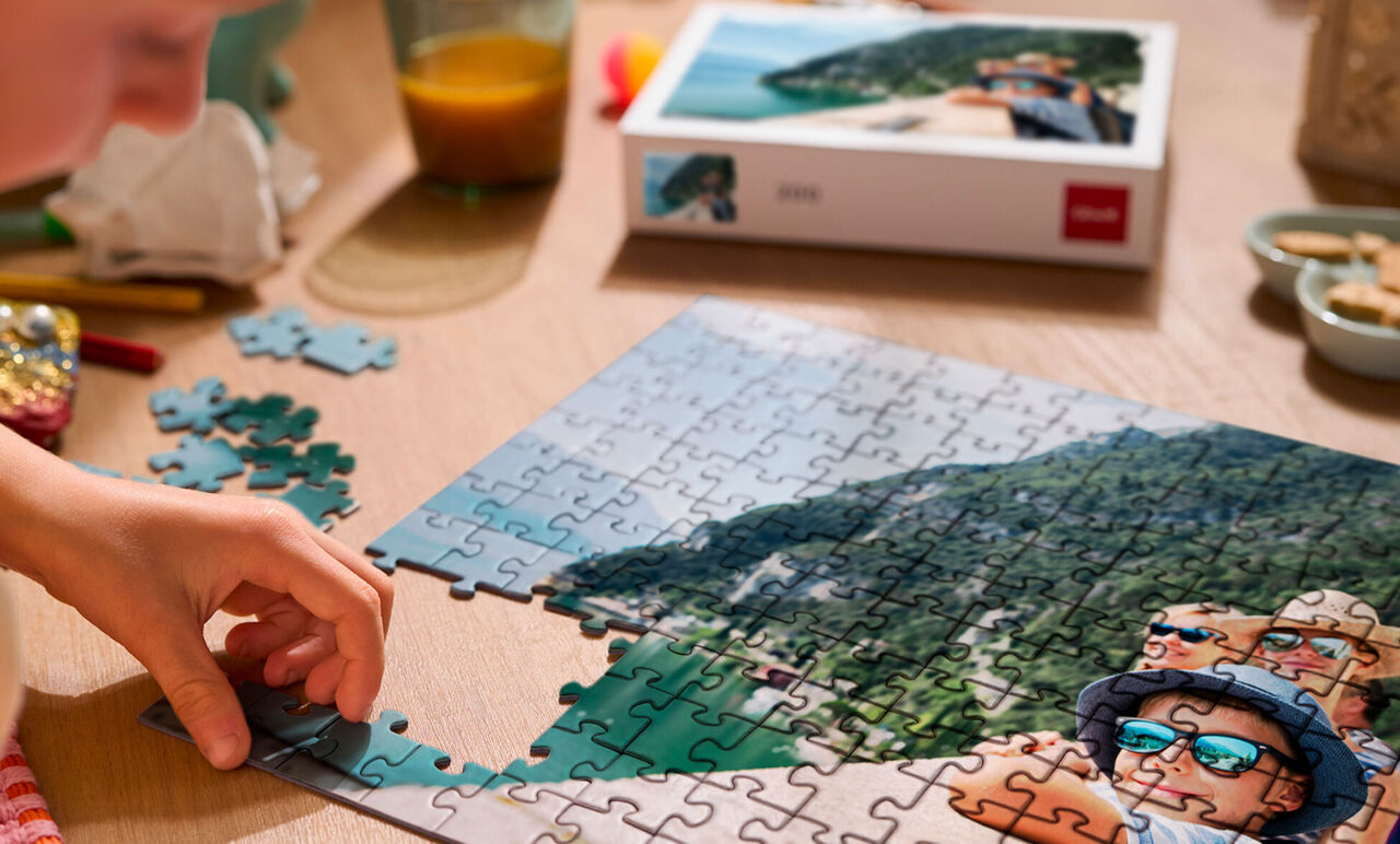 Mano armando un puzzle personalizado con foto de vacaciones familiares sobre una mesa, junto a su caja.