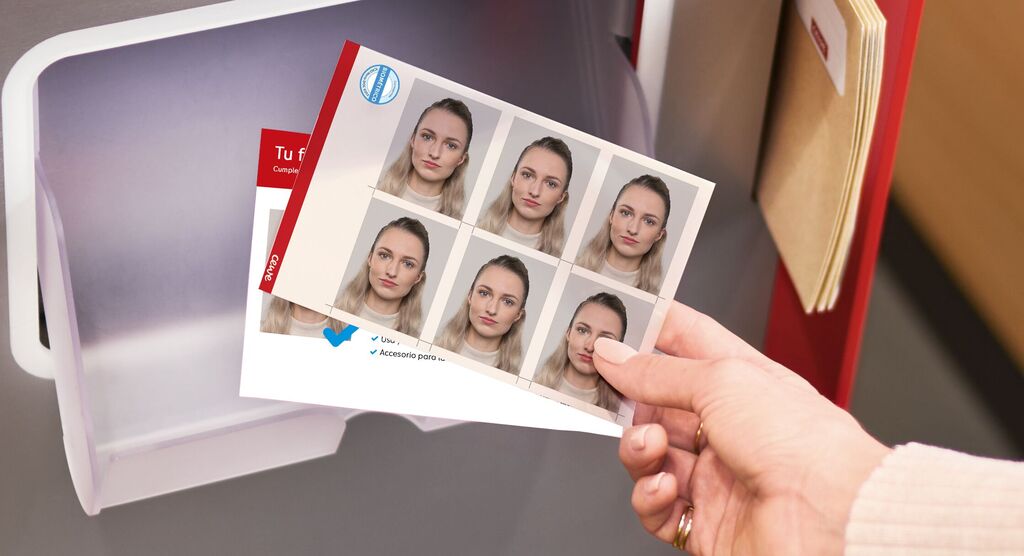 Mano sosteniendo una hoja con varias fotos tipo carnet recién impresas junto a la bandeja de recogida del quiosco.