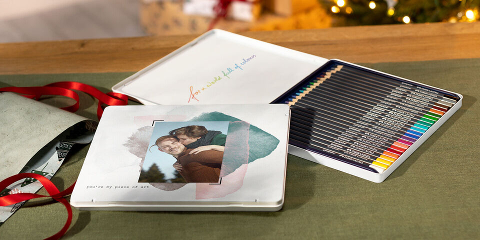 Una elegante caja de regalo de CEWE FOTOBUCH con lápices de colores y una foto de una pareja en la portada