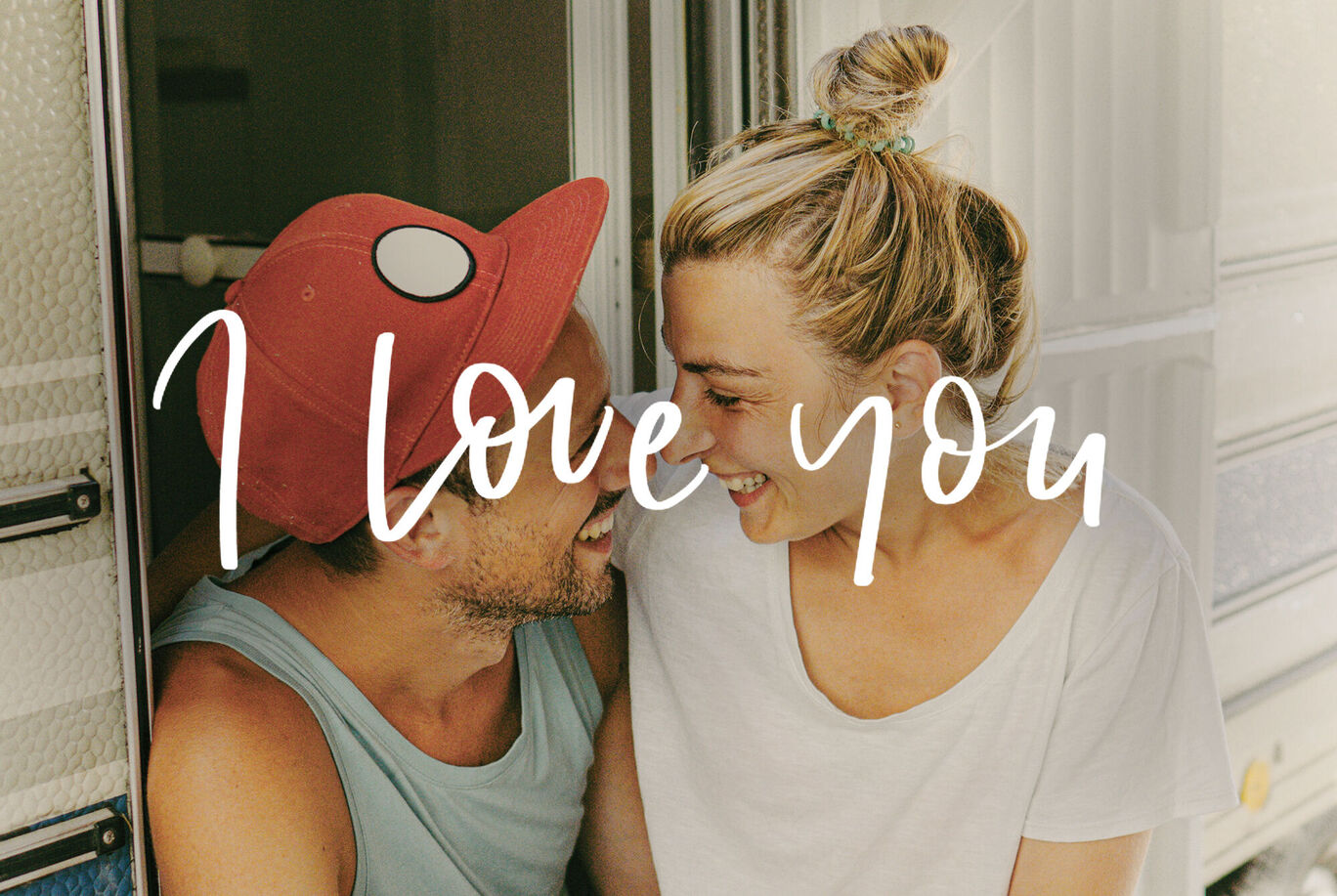 Una pareja sentada en una autocaravana disfrutando de un hermoso momento. Texto 'I Love You' arriba.