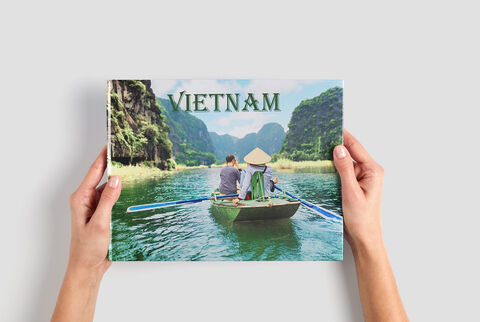 Personas sostienen un CEWE Fotobuch titulado Vietnam en un barco en un paisaje tranquilo.