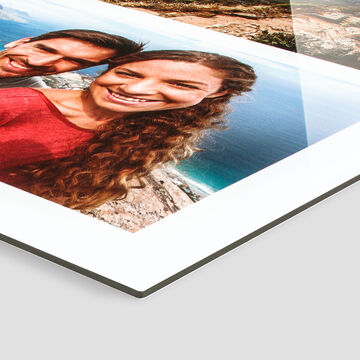 Una pareja feliz sonríe a la cámara, el océano brilla al fondo. Fotolibro CEWE.