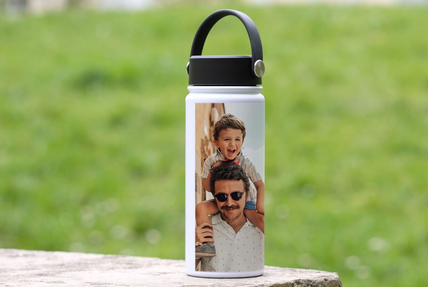 Botella de agua con foto personalizada en un entorno verde.