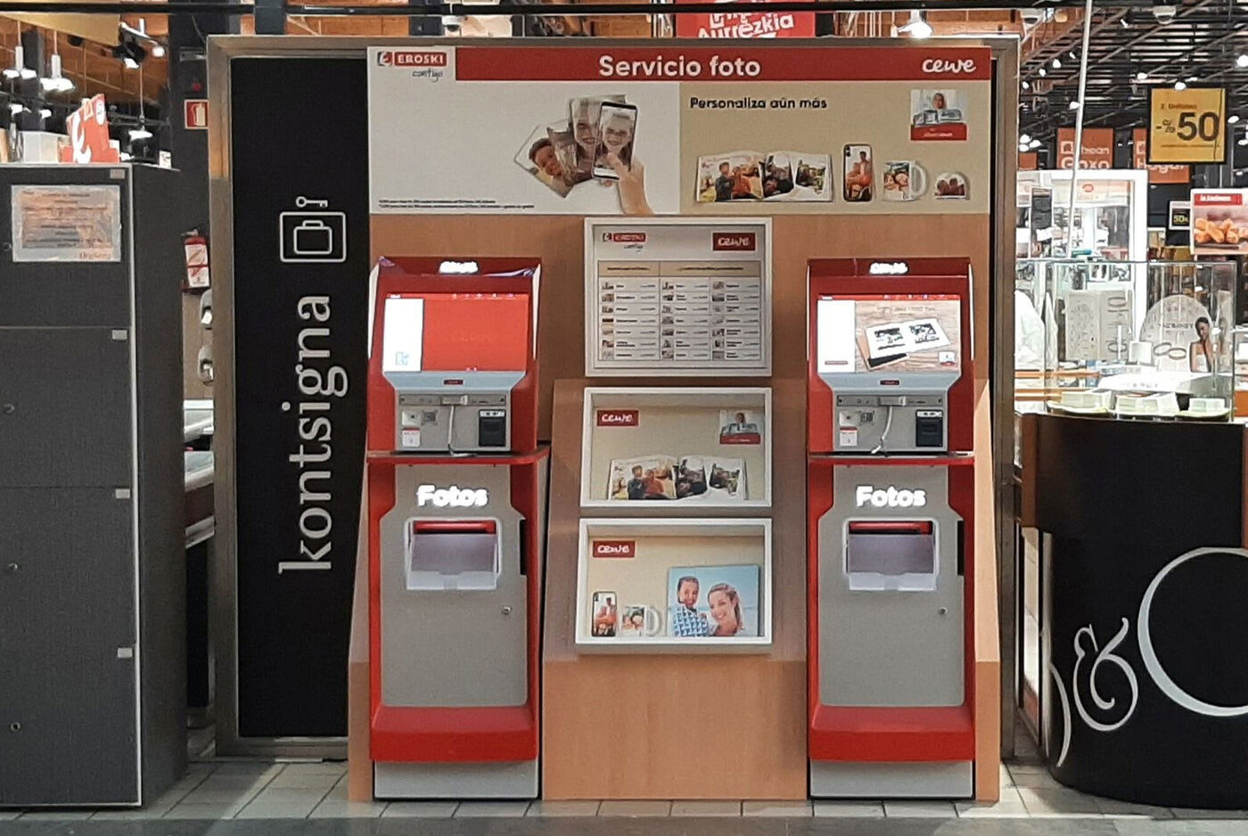 Quiosco de servicio de impresión de fotos CEWE en tienda, con máquinas automáticas y cartelería roja.