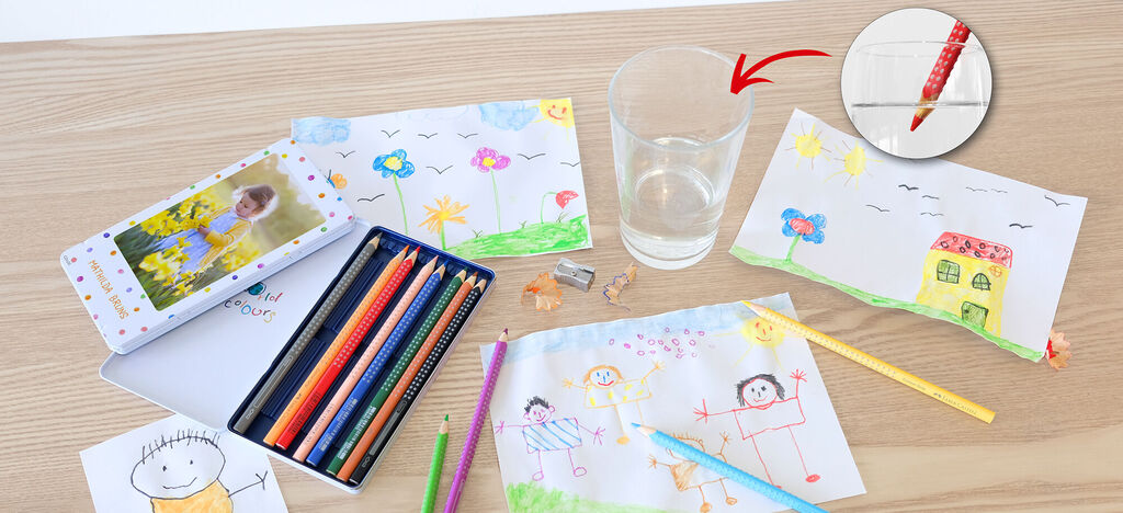 Una mesa con dibujos coloridos, lápices y un vaso de agua.
