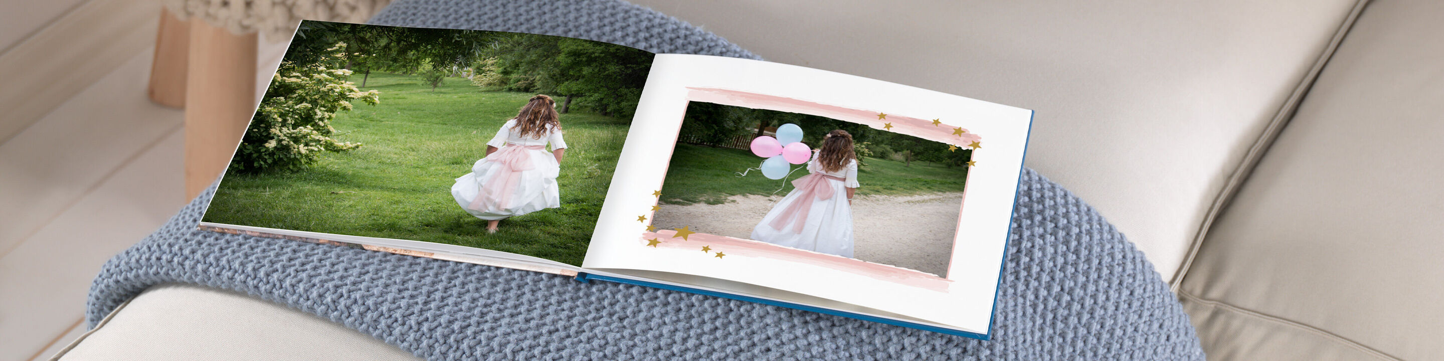 Una niña en un vestido blanco corre feliz por un prado verde, sosteniendo globos de colores. Hay un CEWE Fotobuch con recuerdos cerca.
