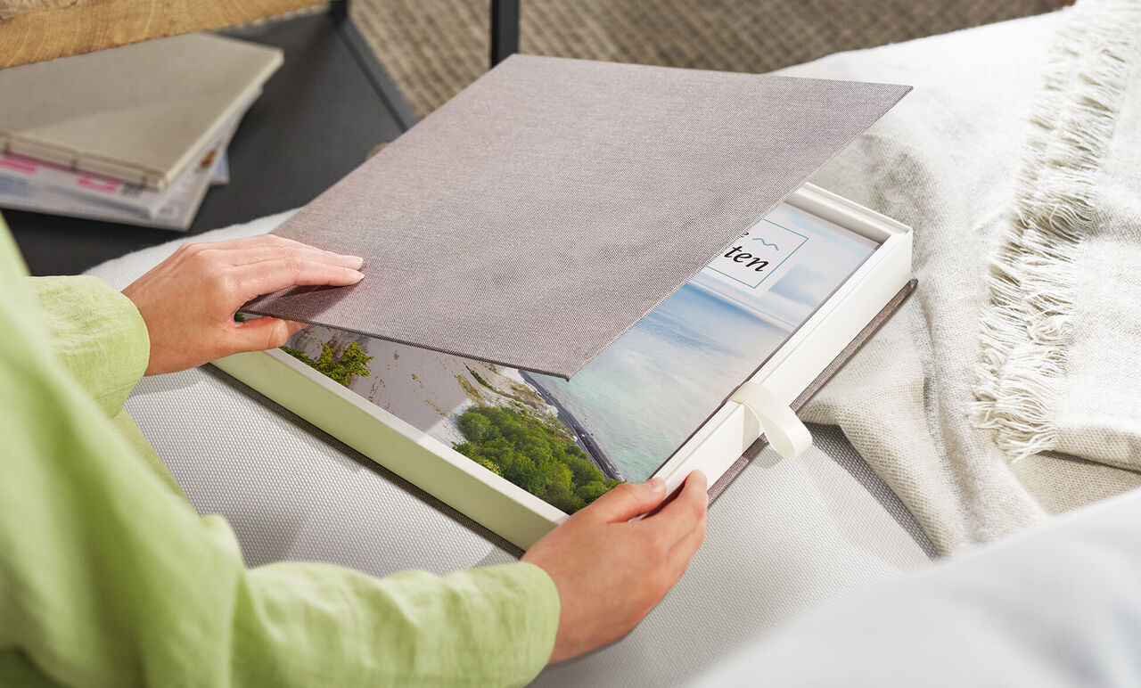 Una persona abre un libro de fotos CEWE en una mesa para ver recuerdos.