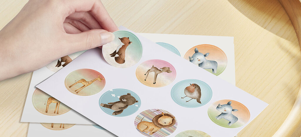 Dos hojas apiladas con pegatinas de animales, una mano sostiene una pegatina.