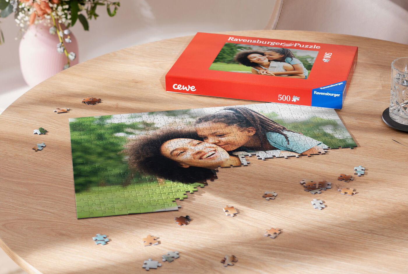 Dos mujeres sonrientes arman un rompecabezas sobre una mesa, al lado está el empaque del rompecabezas CEWE Ravensburger.