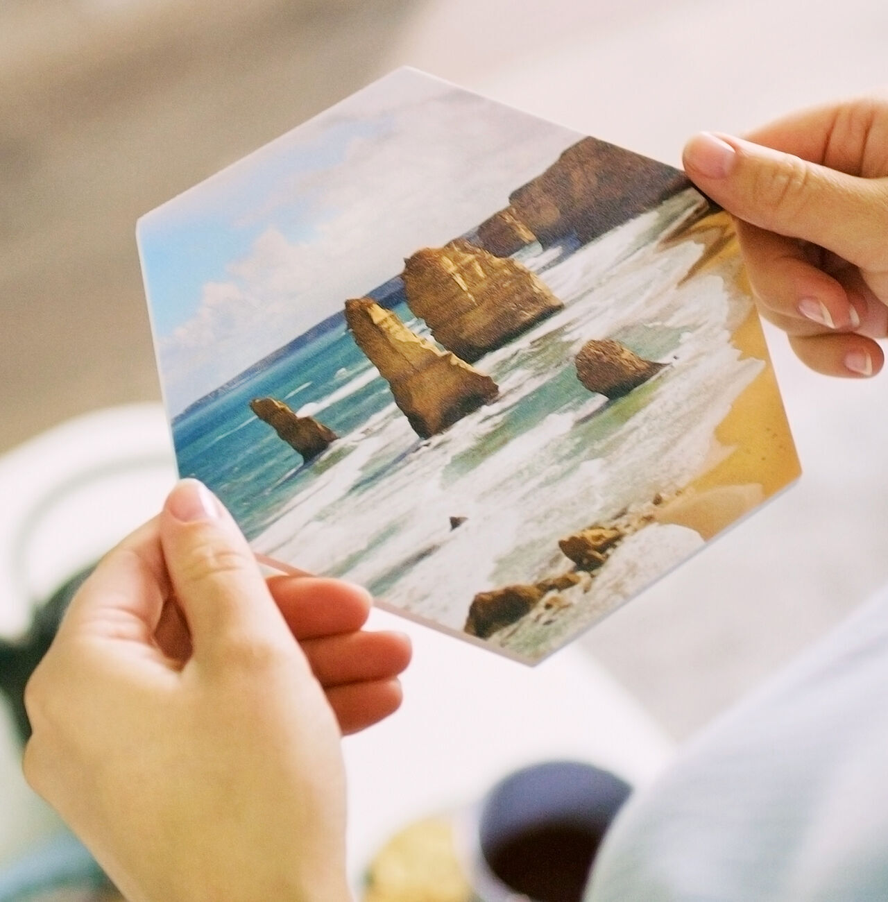 Una persona sostiene una tarjeta fotográfica hexagonal de los famosos Twelve Apostles en la costa australiana.