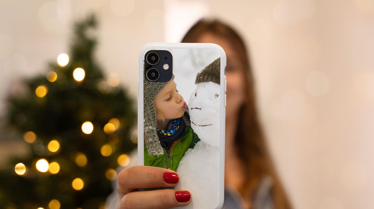 Persona sostiene un teléfono con una foto de una rama nevada y luces brillantes de fondo