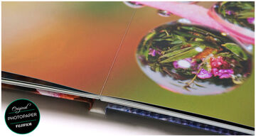 Primer plano de una página de un CEWE FOTOLIBRO con imágenes coloridas y nítidas y una gota de agua.