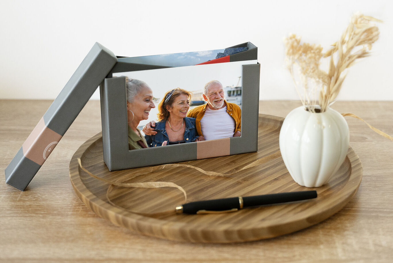 Un marco de fotos con la imagen de amigos, un jarrón elegante y un bolígrafo sobre una bandeja de madera.