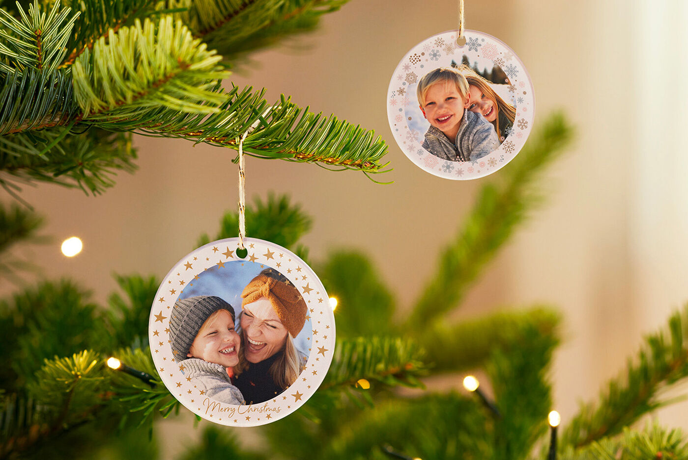 Dos adornos navideños diseñados con amor de papel fotográfico cuelgan de un abeto verde.