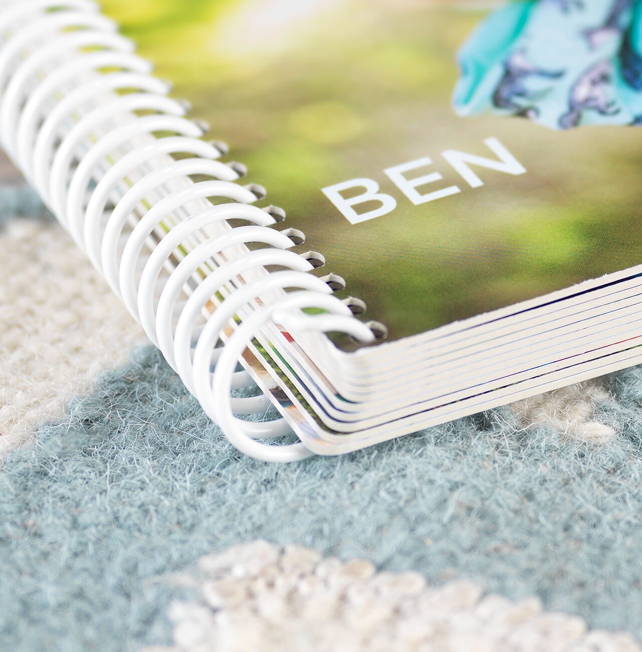 Un CEWE Fotobuch titulado "BEN" sobre una alfombra. La portada muestra un fondo borroso.