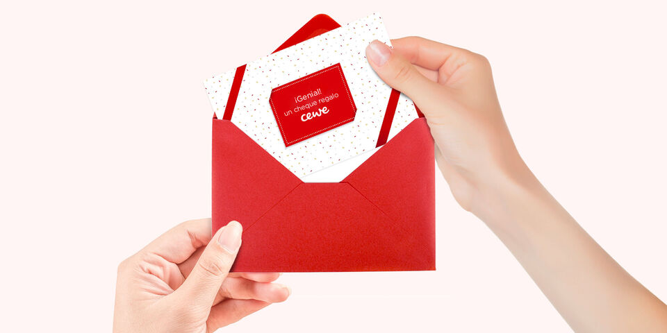 Una mano sostiene un sobre rojo con una tarjeta decorada con puntos y el logo de CEWE.