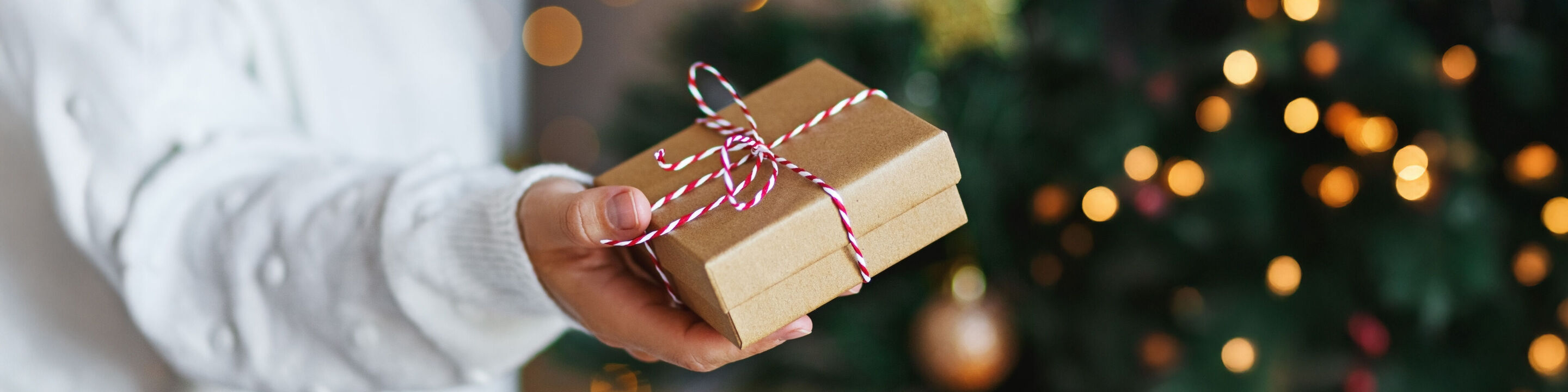 Una persona sostiene un regalo envuelto con amor y un lazo colorido en un fondo decorado festivamente