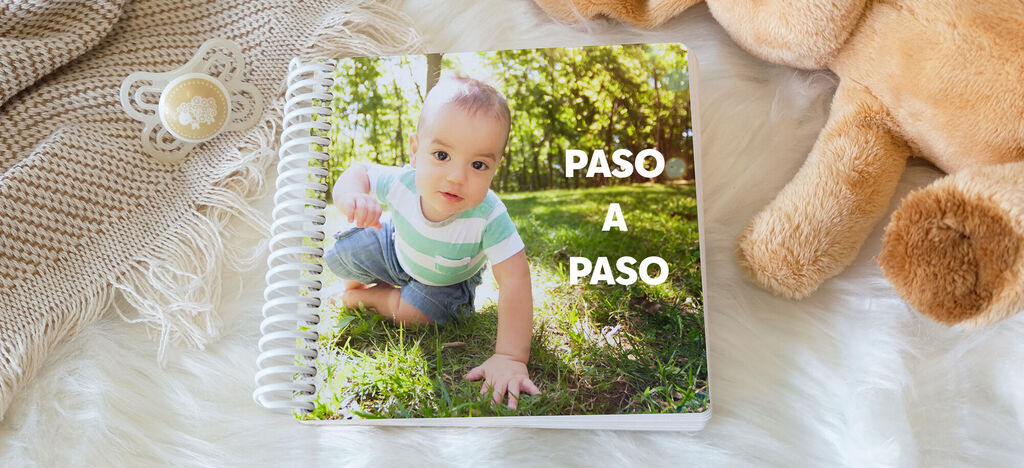 Un niño gatea en una pradera delante de un fotolibro titulado 'Paso a Paso'.