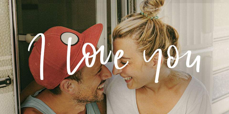 Una pareja disfruta de un momento de intimidad en una autocaravana con un mensaje amoroso en el fondo.