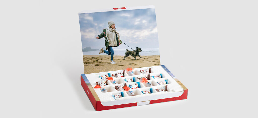 Un niño feliz corre con un perro en la playa, mientras una caja colorida llena de dulces está en primer plano