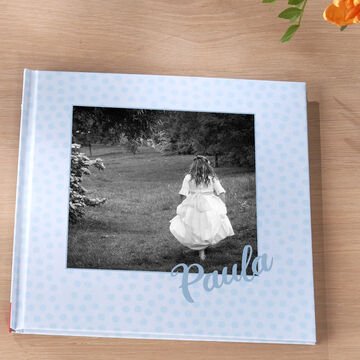 Una niña en un vestido blanco corre sobre un prado con árboles al fondo. En el álbum está el nombre Paula.