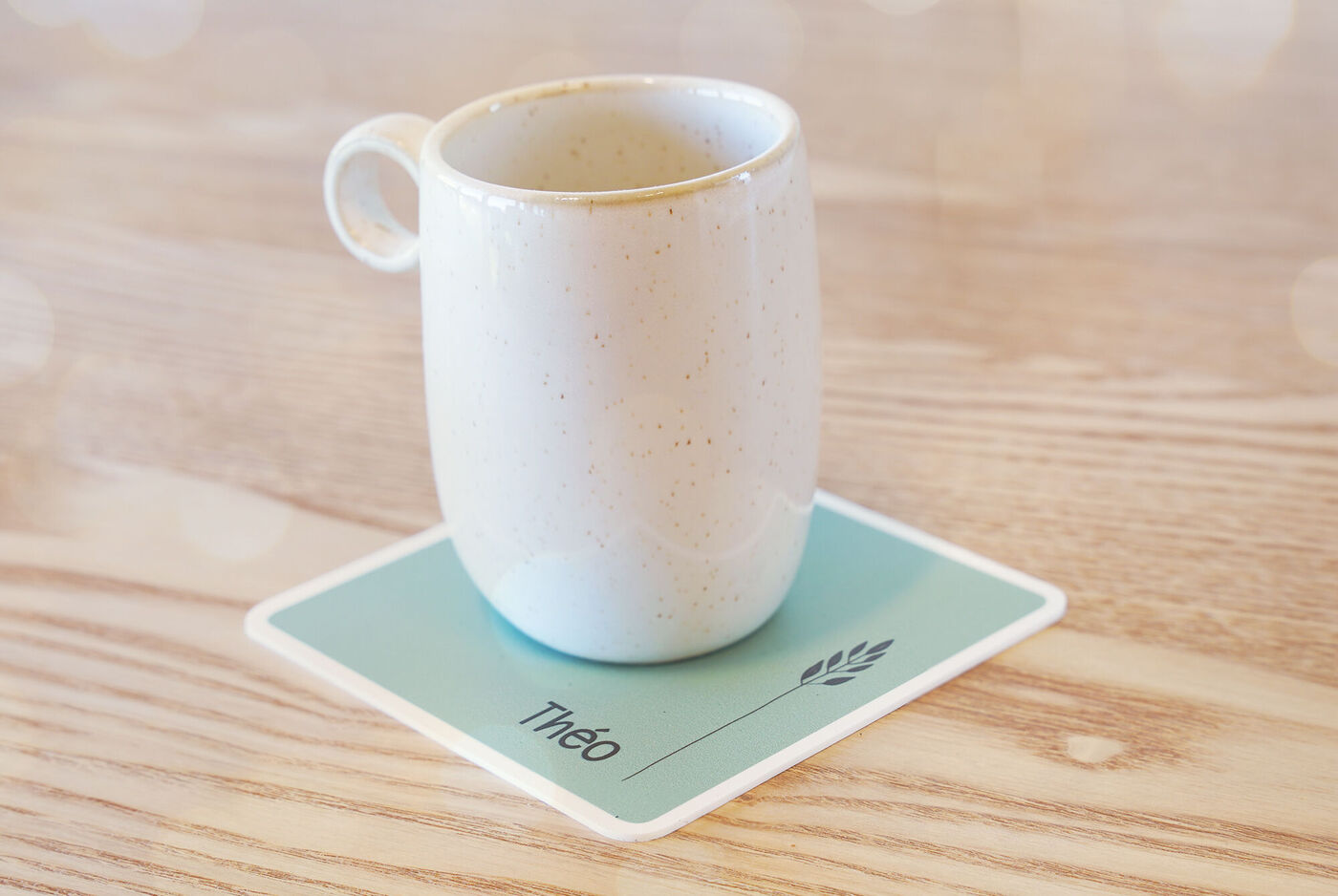 Taza blanca en un posavasos con el nombre 'Théo'.