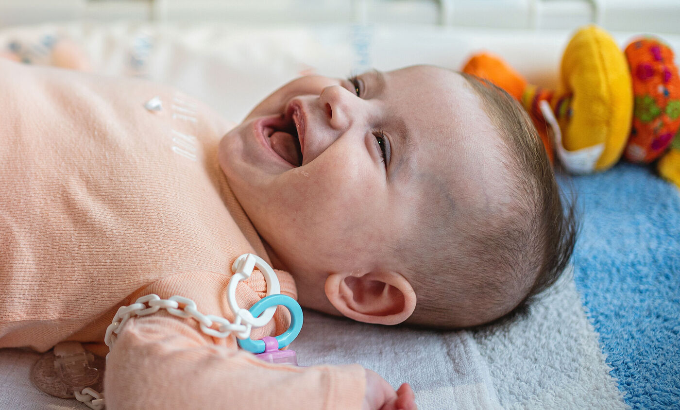 bebé con chupete riéndose dentro de la cuna.