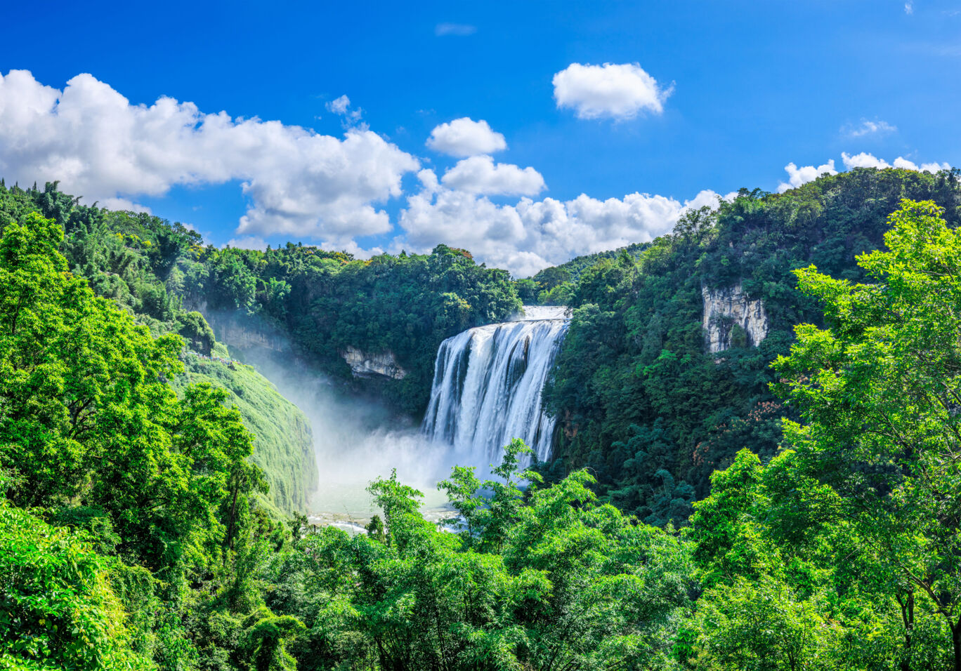Una imagen aérea de un paisaje exuberante con cascada, rodeado de árboles, con el logo CEWE en el centro.