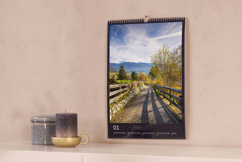 Un calendario de pared hermoso con una foto de un camino entre árboles y montañas.