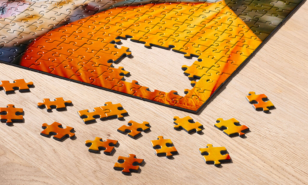 Puzzle de color naranja vibrante en proceso de construcción sobre una mesa de madera clara, mostrando el área central vacía y piezas sueltas