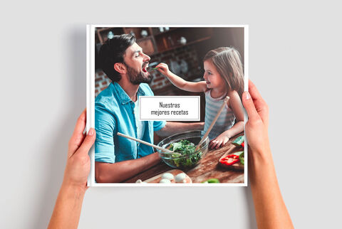 Una persona sostiene un libro de cocina, con un niño añadiendo verduras a un tazón.