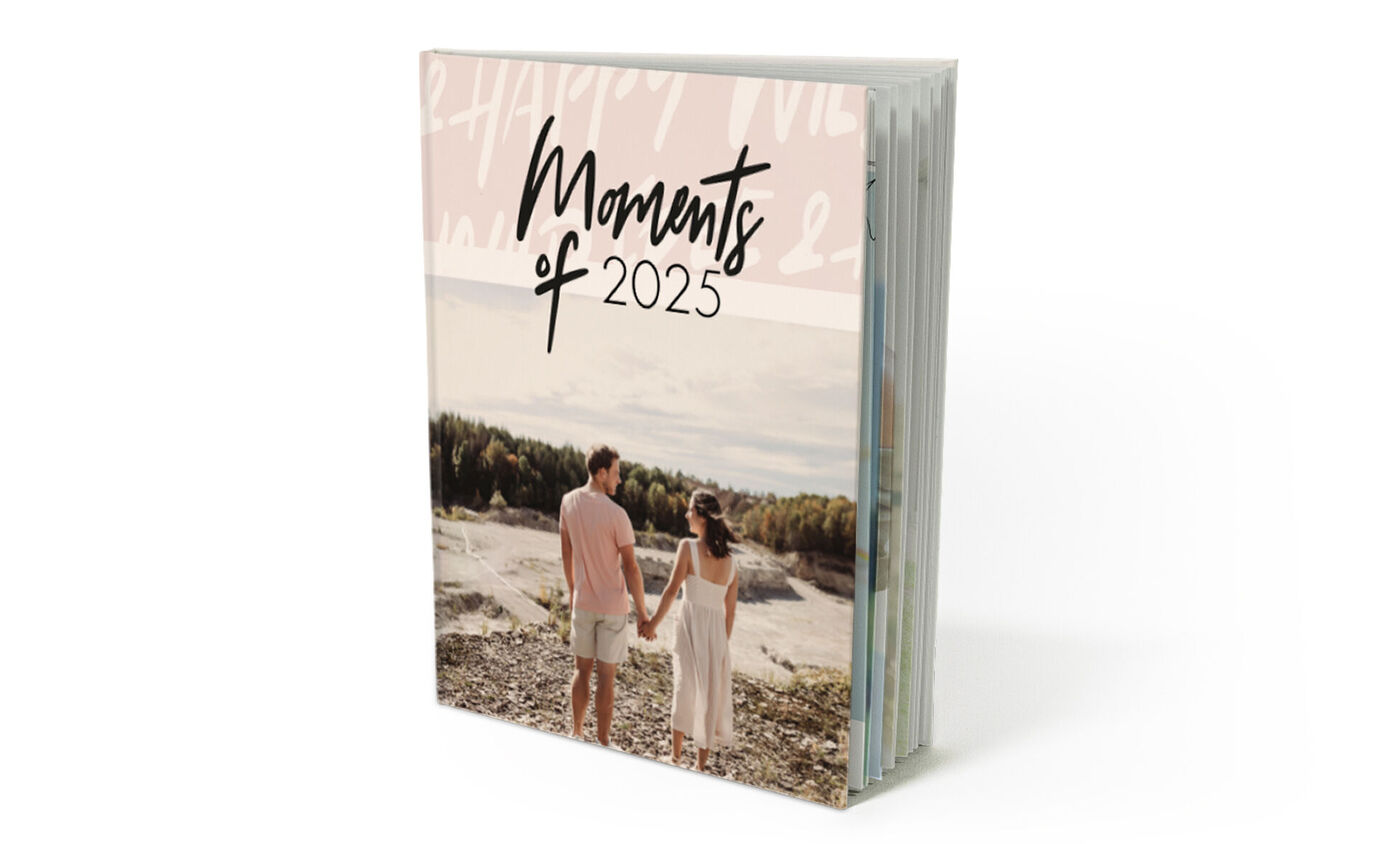 Una pareja feliz toma de la mano y mira el paisaje en la portada de un CEWE fotolibro titulado "Momentos de 2024".