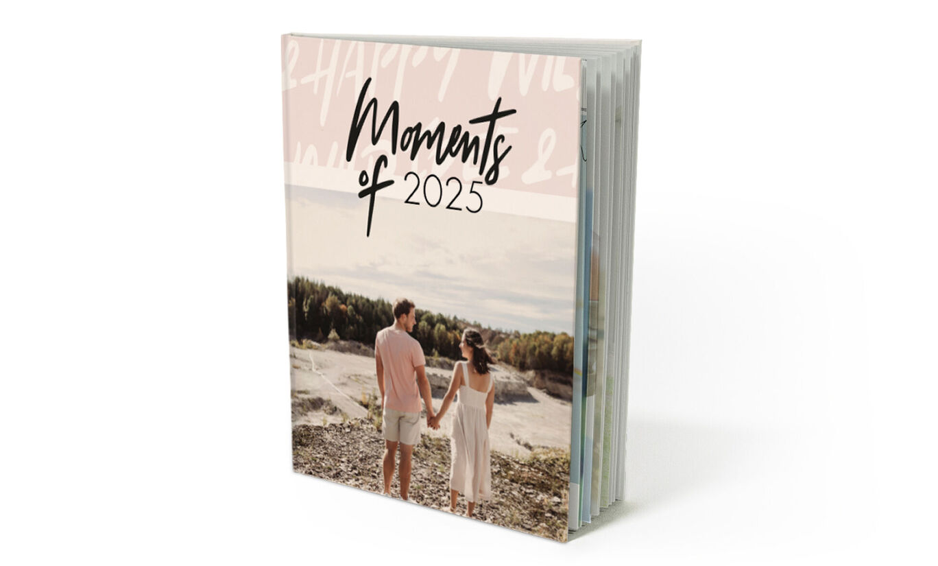Una pareja feliz toma de la mano y mira el paisaje en la portada de un CEWE fotolibro titulado "Momentos de 2024".