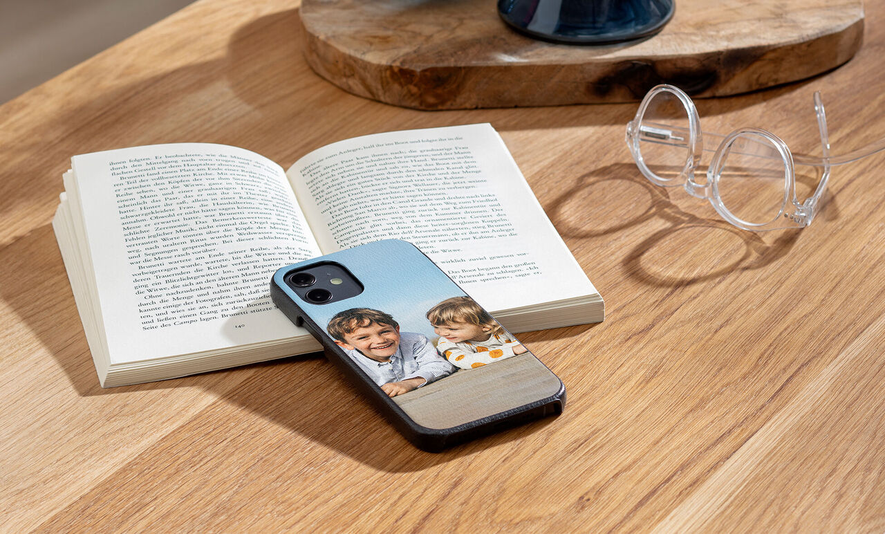 Un libro abierto sobre una mesa con un smartphone y dos niños riendo en la cubierta.